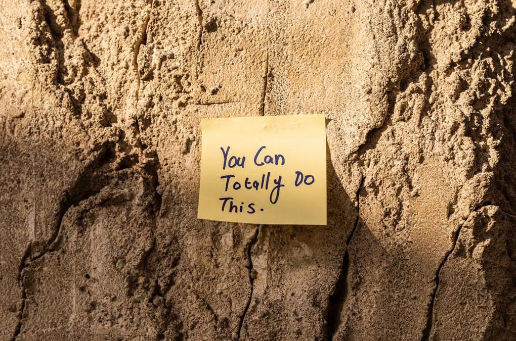 A sticky note with a motivational message on a textured wall in Dubai, with sunlight casting shadows.